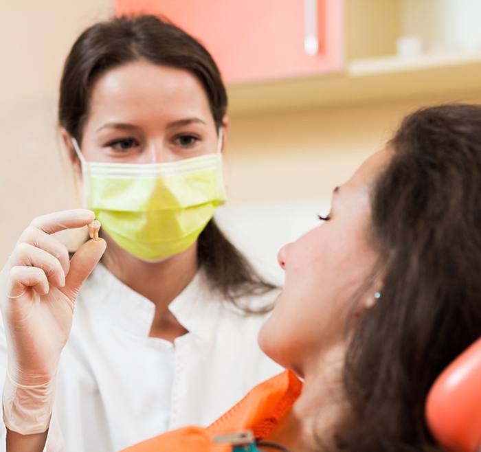 Dental team member showing extracted tooth to patient