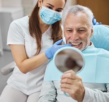 Happy dental patient admiring his new teeth in mirror