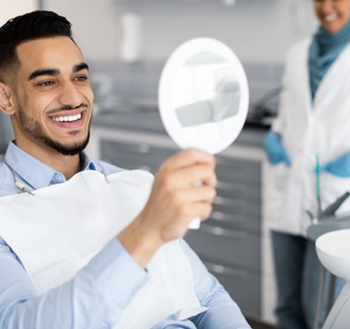 Man smiling at reflection in handheld mirror