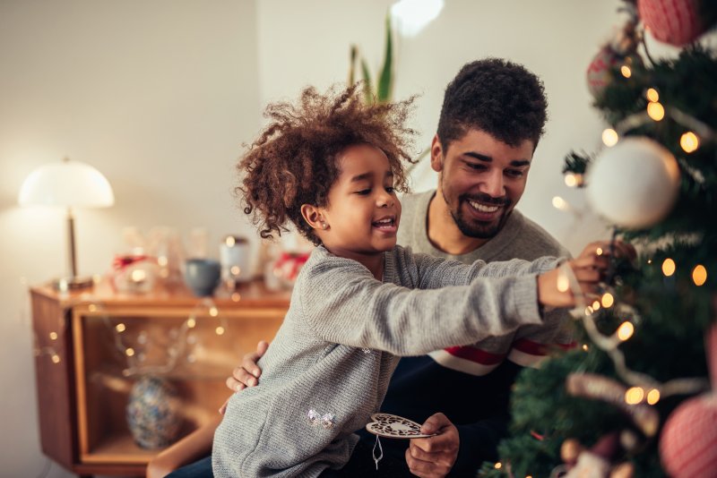Father decorating holiday tree with daughter after root canal